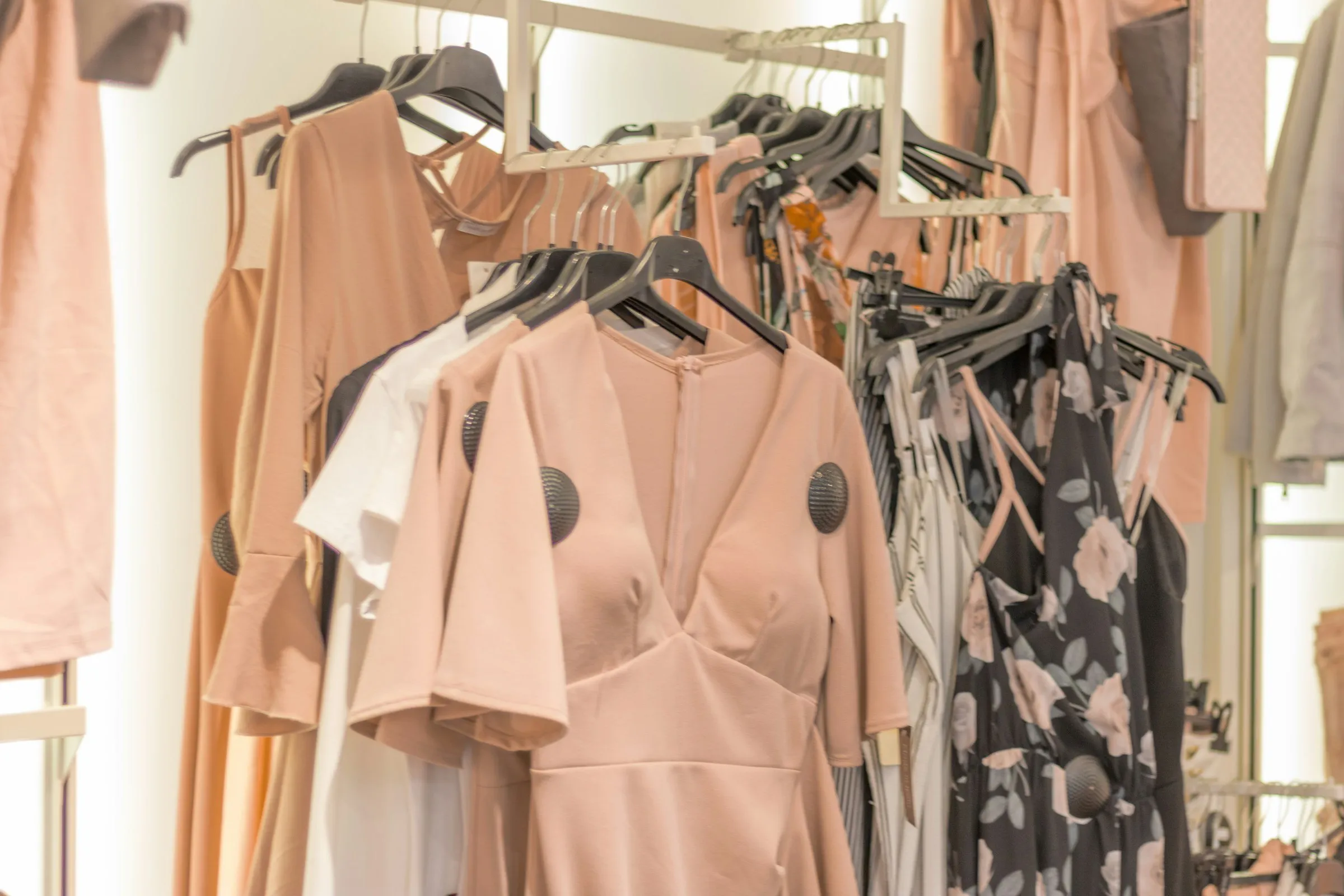 Arara de loja com vestidos em tons de rosa e bege prontos para envio